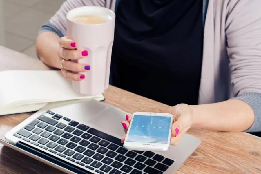 A laptop and a phone on a desk beside a cup of coffee